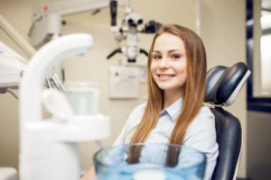 Smiling young woman in a dental chair at Smiles of Chevy Chase, with dental equipment and tools visible, emphasizing patient care and comfort in a dental office setting.