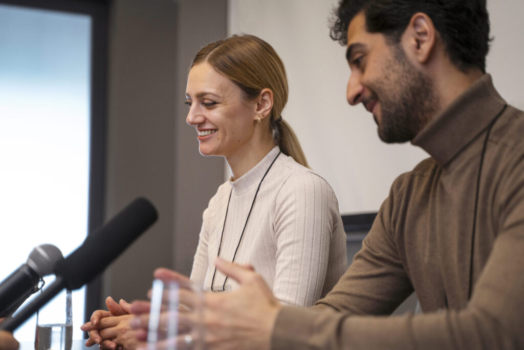 Smiling woman and man seated at a table with microphones, engaged in discussion, emphasizing comfort and communication in a professional setting.
