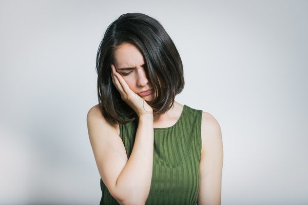 Woman experiencing jaw pain, holding her face in discomfort, illustrating symptoms relevant to periodontal issues and ARESTIN treatment.